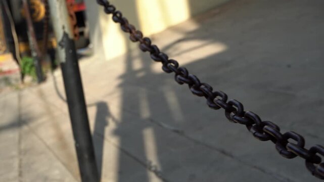 Dynamic motion shot of a swaying metal chain barrier outdoors on a sunny day in the historic old town district of Gresik, East Java, Indonesia.