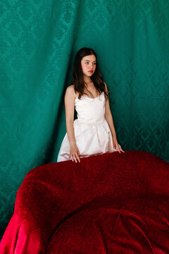 Woman in white dress standing behind a red velvet couch