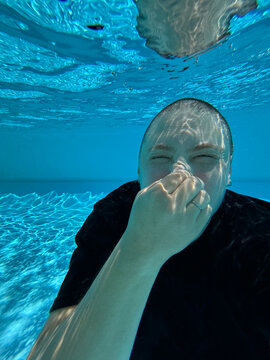 Person Swims Underwater While Holding Nose in a Clear Pool