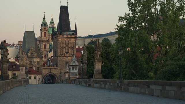 Empty Charles Bridge in Prague during early morning light with Lesser Town tower view. Historic cobblestone walkway features gothic architecture. Perfect for European travel and tourism.