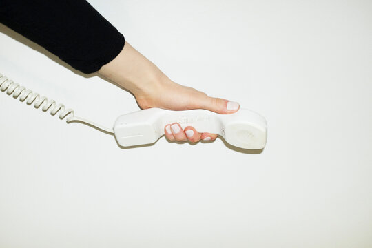 Hand holding white landline phone with curvy wire with flashlight