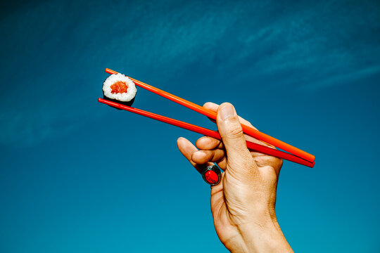 a man raises red chopsticks holding a salmon sushi roll
