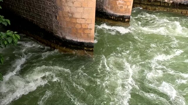 Turbulent Water Gushing Through Stone Dam Pillars With White Foam