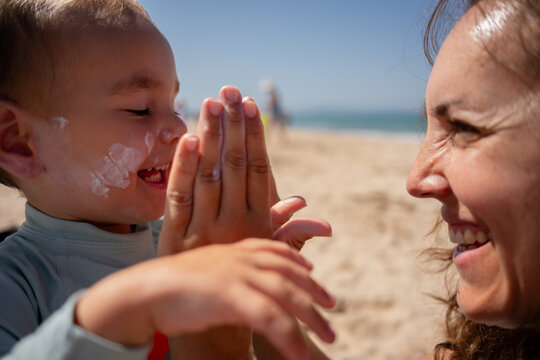 Mother applying sunscreen to happy son at beach
