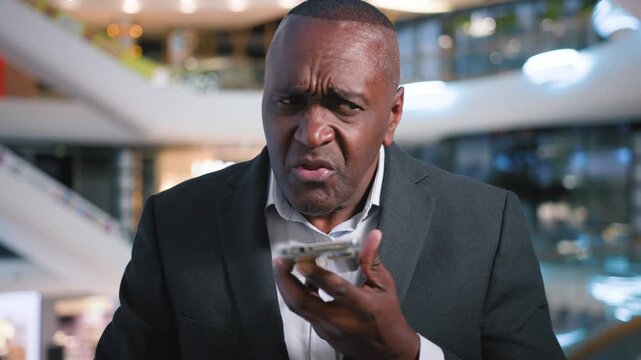 Serious worried 50s African American business man talking mobile phone audio message call ethnic businessman male executive talking negative anxious record voice mail talk with smartphone loudspeaker