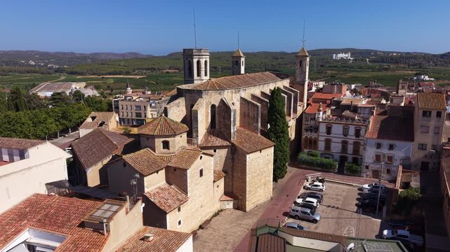 Aerial view of Church of Sant Julia in l'Arboc, Catalonia, Spain, featuring three octagonal towers and tiled roofline above town rooftops, with vineyards and farmland stretching to distant hills