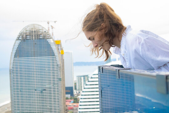 Scared woman looking down from skyscraper balcony suffering from fear of heights.