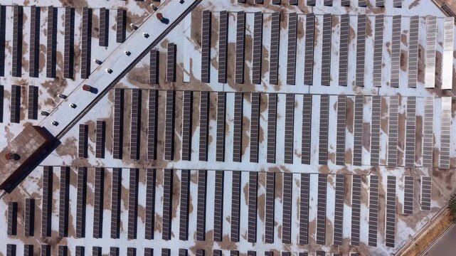 Overhead view of diagonally aligned rows of photovoltaic solar panels on a large industrial rooftop with maintenance walkway and surface soiling patterns forming bold repeating graphic texture