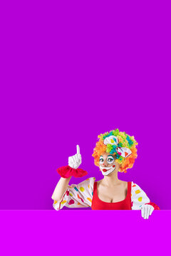 Funny female clown pointing up at blank template copy spase for advertising, posters, greetings, invitations. Entertainer as Joker in a suit and wig, with clown whiteface makeup