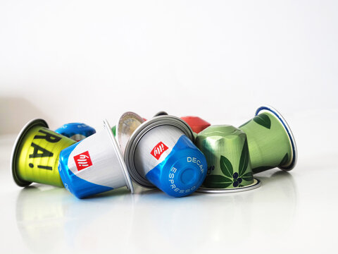 A pile of assorted colorful coffee capsules including illy decaf and green capsa pods lying on a white surface with a clean background.