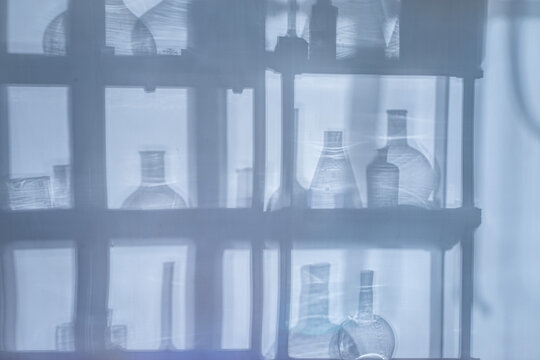 Abstract background with shadows of laboratory equipment and glassware projected on a surface, blue cinematic lighting, science backdrop with copy space.