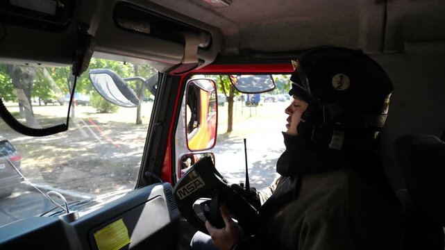 Professional fireman in uniform riding on a big truck to place of a fire. Young male firefighter in full equipment driving on fire engine to an emergency. Concept of saving lives and heroic profession