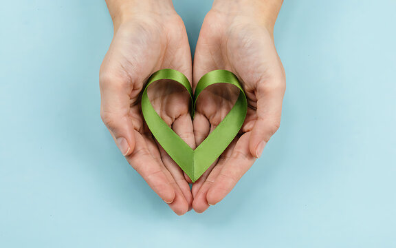Hands holding a green ribbon shaped like a heart representing mental health awareness and support