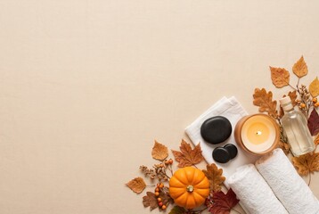 Different spa items are arranged neatly on a beige background. There are candles, towels, smooth stones, and autumn leaves. A small pumpkin adds to the seasonal decor