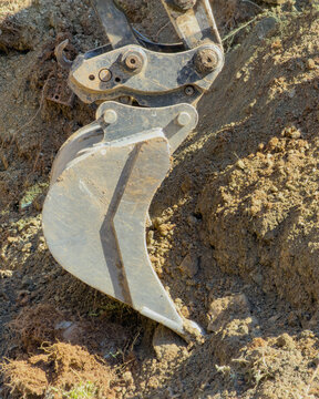 Hydraulic excavator bucket digging compacted earth during an active outdoor construction operation