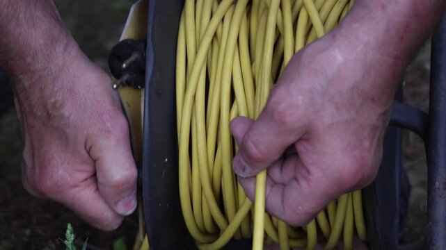 Male worker hands winding yellow electrical cable onto a spool, slow motion