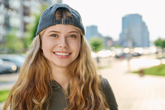 Portrait of pretty smiling blonde teen girl wearing backward baseball cap outdoors
