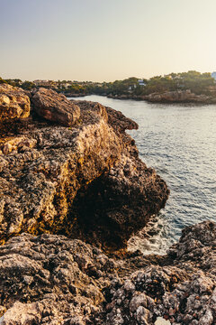 Sunlit rocky shoreline in scenic Cala d'Or, Mallorca, Spain.