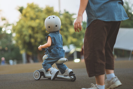 Toddler riding a three wheel scooter outdoors with an adult walking beside, active childhood, outdoor play and early mobility development