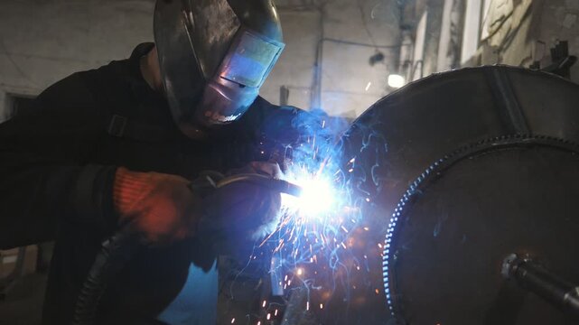 Worker in protective mask welding metal construction. Welder doing joint between two steel details. Man welding parts of the metal detail together. Industrial production manufacture. Close up