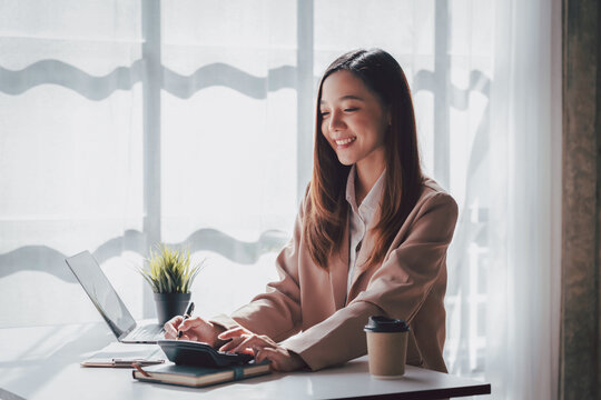 Asian Women Accounting on Calculator with Laptop and Coffee Cup in Office - Financial Analysis Budgeting Taxes for Small Business and Remote Work Lifestyle