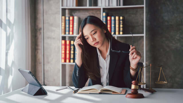 Exhausted Asian Female Lawyer Overwhelmed by Legal Case Work at Office Desk with Law Books, Scales of Justice, Gavel and Tablet for Attorney Concept