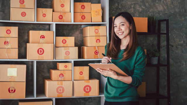 Asian Woman Checking Stock Inventory for Online Business and E-Commerce Store Preparing Orders for Delivery Shipping Boxes and Parcel Packages