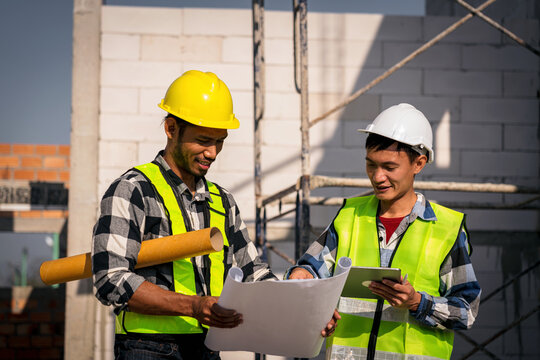 Asian Construction Workers Reviewing Blueprints on Building Site Safety First Young Men Planning and Discussing Project Details Wearing Hard Hats and Vest