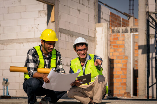 Adult Asian Construction Workers Reviewing Blueprint at Construction Site Wearing Hard Hats and Safety Vest Building Architecture Real Estate Project Development