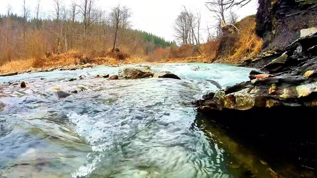 A view of a clear, fast-flowing river amidst lush wilderness, featuring the soothing sound of murmuring water, a mountain forest landscape, and rocky cliffs.