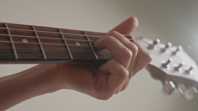 Closeup left hand forming guitar chords on fretboard, backlit studio glow, precise fretting, chord progression sketching, songwriting practice, soft ballad mood, wrist posture, capo visible, intimate