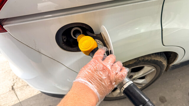 Gloved hand refueling a white car at a petrol station in daylight, clean safety focused image suitable for automotive editorial, fuel industry marketing, social media posts