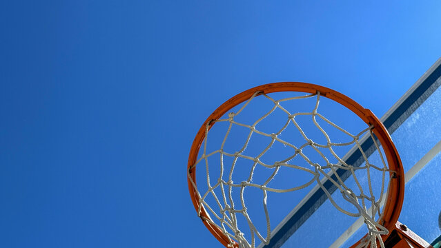 Close up of an outdoor basketball hoop against a clear blue sky with bright summer sunlight, energetic sports mood suitable for sports editorial, athletic marketing, social media
