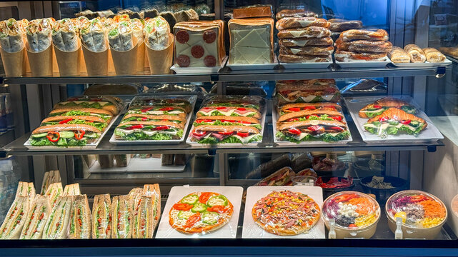 Brightly lit gourmet deli display in a modern cafe showcasing sandwiches pizzas and salads in a glass case suitable for restaurant menus, food blogs, social media