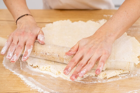 Baking process. Rolling dough pin. Female chef hand flattening sweet mass on home wooden kitchen table covered with flour making pastry.