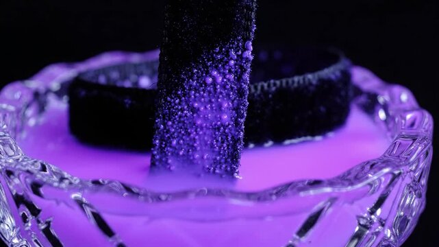 Spooky Halloween potion bubbling in a crystal glass bowl with neon purple liquid and a textured black element dipped inside for a gothic mood