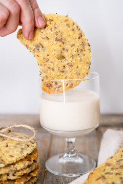 Eating cookies. Healthy food. Woman hand dipping bitten crispbread treat with flax pumpkin seeds in white yogurt glass on wooden table.