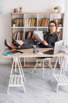 Professional workflow. Office worker. Confident female boss working with business document notebook using laptop at modern desk indoor.