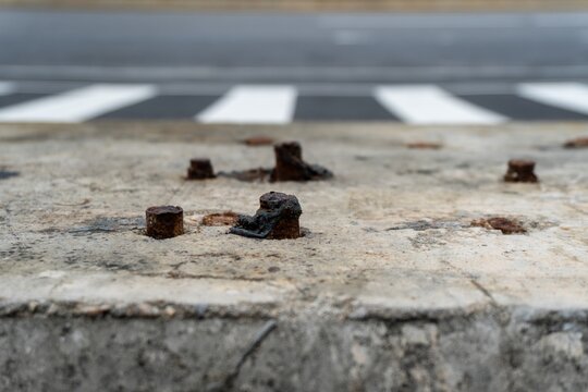 Rusty bolts embedded in concrete near pedestrian crossing