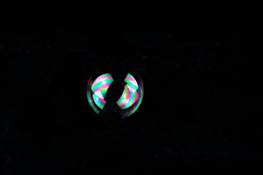 Macro shot of a vibrant, iridescent soap bubble resting against a solid black background. 