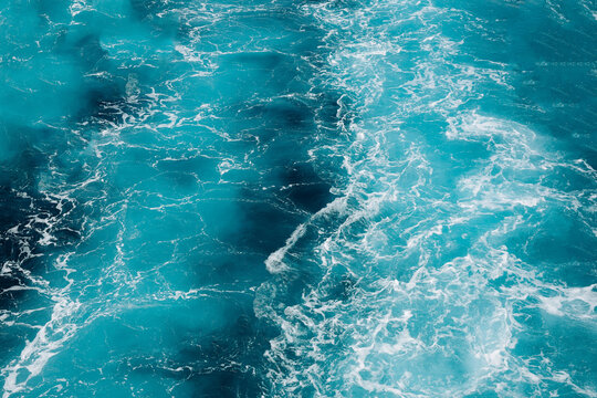 Turquoise ocean water with white foamy waves creating a natural abstract texture and vibrant blue background.