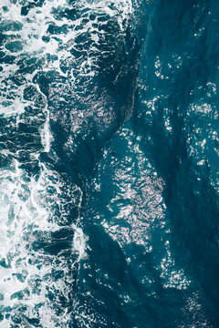 Abstract aerial texture of crystal blue ocean water with swirling waves and white sea foam.