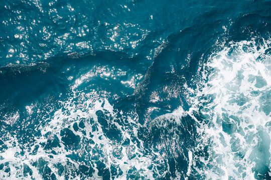 Abstract aerial texture of crystal blue ocean water with swirling waves and white sea foam.