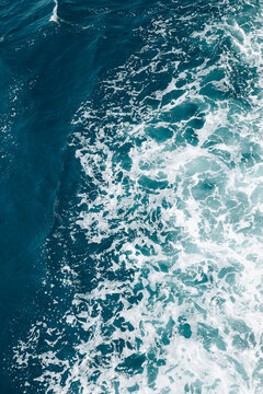 Turquoise ocean water with white foamy waves creating a natural abstract texture and vibrant blue background.