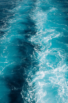 Turquoise ocean water with white foamy waves creating a natural abstract texture and vibrant blue background.
