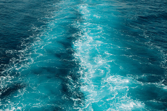 Abstract aerial texture of crystal blue ocean water with swirling waves and white sea foam.