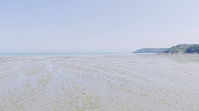 Wide static shot of Binic beach at low tide on a clear summer day, with gentle ripples in the wet sand and calm shallow water stretching towards the horizon.