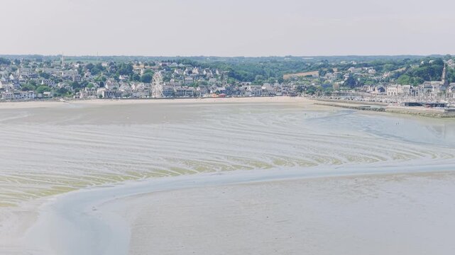 Aerial view of the coastal town of Binic in Brittany, France, with its sandy beach, harbor, and waterfront buildings visible at low tide.