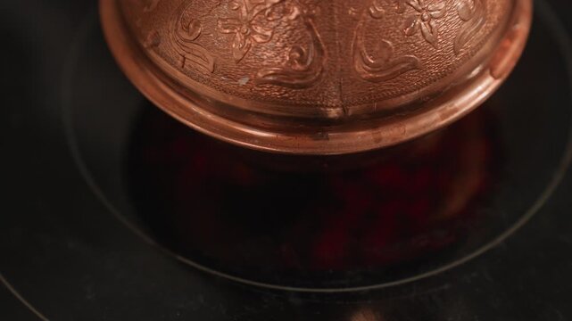 Ornate cezve over red burner closeup brewing motion with bubbling coffee, copper embossing, glossy cooktop reflection, rising steam, ritual tension, artisan barista vibe for coffee lover