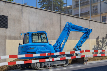Road excavator leveling sand on a sidewalk during street construction, surrounded by red and white safety barriers © Irina